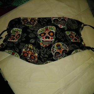 May include: Black face mask with a colorful sugar skull pattern. The mask has black elastic ear loops.