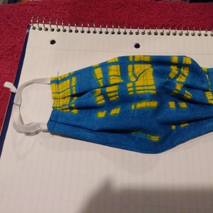 May include: A blue and yellow patterned face mask with white elastic ear loops.