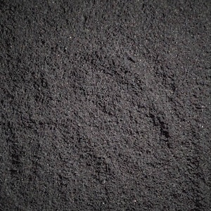 May include: A close-up of a black, granular substance. The texture is fine and uniform, resembling a powder or fine sand.