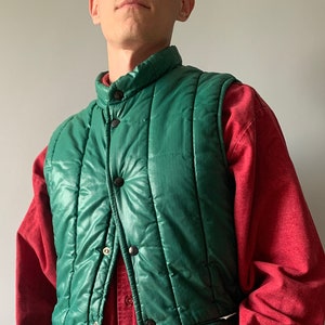 Pode incluir: Um colete acolchoado verde com fecho de pressão. O colete tem um colarinho alto e é feito de um material brilhante.