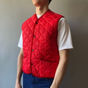 May include: A red quilted vest with a button closure and a pocket on the front. The vest has a diamond pattern and a corduroy trim.