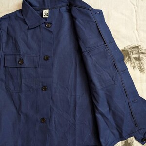 May include: A navy blue button-down shirt with two chest pockets and a collar. The shirt has black buttons and a relaxed fit. The fabric appears to be a lightweight material, suitable for warmer weather.