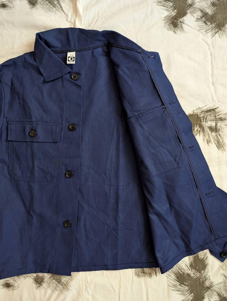 May include: A navy blue button-down shirt with two chest pockets and a collar. The shirt has black buttons and a relaxed fit. The fabric appears to be a lightweight material, suitable for warmer weather.