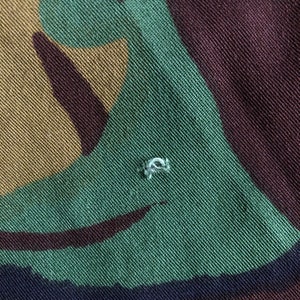 May include: Close-up of a green, brown, and black camouflage fabric with a small white thread loop.