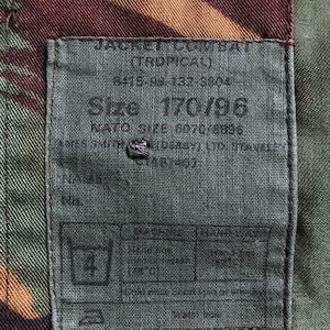 May include: A green, brown, and tan camouflage fabric with a gray label sewn on. The label has black text that reads "Size 70/86".