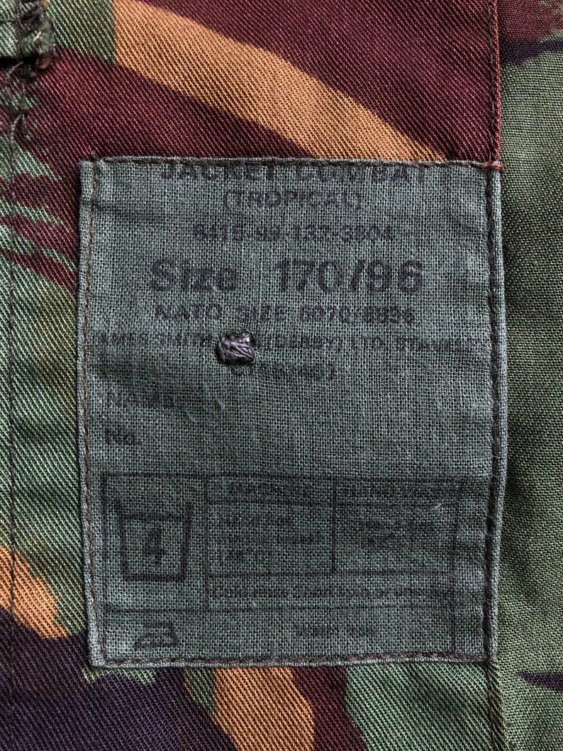 May include: A green, brown, and tan camouflage fabric with a gray label sewn on. The label has black text that reads "Size 70/86".