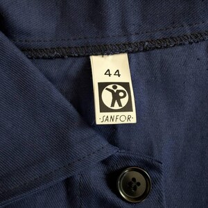May include: Close-up of a navy blue work shirt with a black button and a label that reads "44" and "SANFOR". The label features a graphic of a person with outstretched arms.