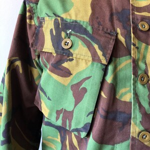 May include: A green, brown, and black camouflage long-sleeve shirt with a button-up front.