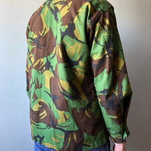May include: A green, brown, and black camouflage jacket with long sleeves and a button-up front.