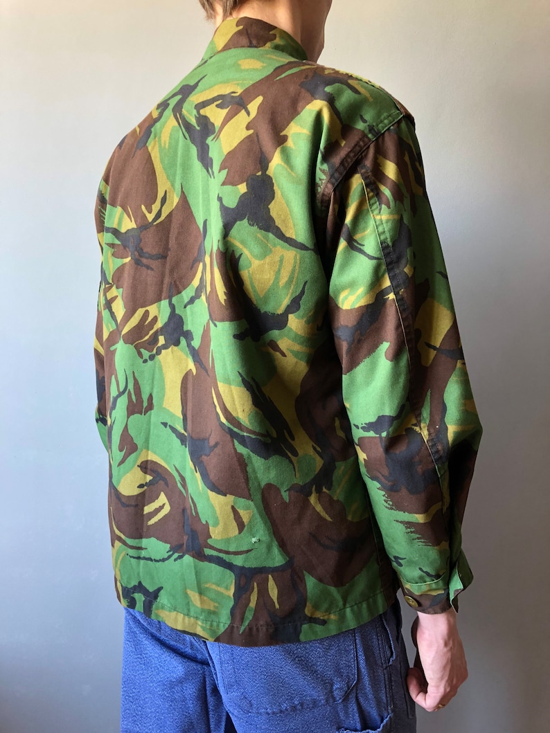 May include: A green, brown, and black camouflage jacket with long sleeves and a button-up front.