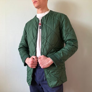 May include: A dark green quilted jacket with a zipper closure. The jacket has a diamond pattern and a ribbed collar and cuffs.