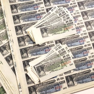 May include: A collection of vintage New York Central Railroad Company stock certificates featuring black and white portraits of a woman, printed text, and various dates ranging from 1974 to 1987, with some certificates stacked on top of a larger sheet.