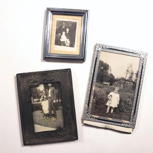 May include: Three vintage framed photographs. The top photo shows a family of three, a man, a woman, and a child. The middle photo shows a man and a child standing in front of a building. The bottom photo shows a child standing in a garden.