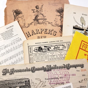 May include: A collection of vintage ephemera, including sheet music, a Harper's New magazine cover, a Baugh's Farmers' Almanac for 1912, and a St. Francis County Railroad Company check. The items are aged with a sepia tone.