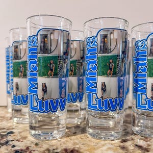 May include: A collection of clear shot glasses with a blue and white design. Each glass features the name "Miah" and the word "Luvv" in a stylized font, along with a photo collage. The number "22" is also displayed.
