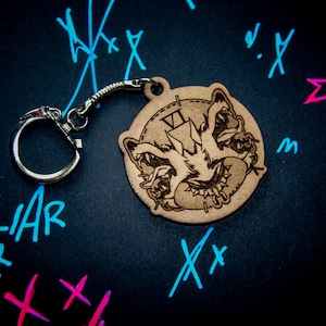 Peut inclure: Un porte-clés en bois avec une sculpture détaillée d'une créature grincheuse avec un cadran d'horloge. Le porte-clés est attaché à un anneau brisé argenté.