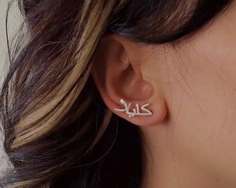 May include: Silver earrings with the Arabic word "Khalid" written in a stylized font.