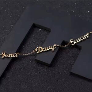 May include: A gold necklace with three names on it: Jena, Dawy, and Suwan. The names are written in a cursive font.