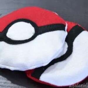 Może przedstawiać: Pluszowa zabawka Pokeball w kolorze czerwonym, białym i czarnym. Sferyczna zabawka ma duży biały okrąg z czarnym obrysem. Miękka zabawka z tkaniny została zaprojektowana tak, aby przypominać kultową piłkę z popularnego serialu animowanego.
