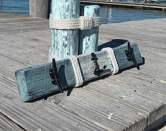 Peut inclure: Un porte-manteau en bois rustique sur le thème nautique. Le porte-manteau est peint en bleu clair et présente des accents de corde et trois crochets en métal noir en forme d'ancres. Le porte-manteau est présenté sur une jetée en bois.