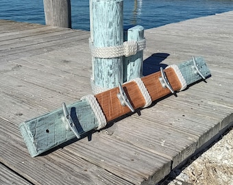 Peut inclure: Un porte-manteau mural en bois rustique avec quatre taquets métalliques. Le porte-manteau présente des sections alternées de bois bleu et marron patinés, enveloppées de corde blanche. Un poteau assorti est en arrière-plan.