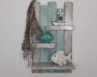 May include: A three-tiered wooden shelf with a distressed white and blue paint finish. The shelf is decorated with a small white sailboat, a turquoise fish, and a white fish. A brown fishing net hangs from the top shelf.