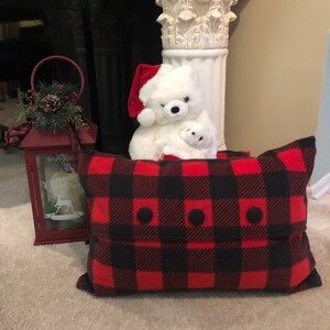 May include: A red and black plaid pillow with three black buttons. The pillow is sitting in front of a white teddy bear wearing a Santa hat.