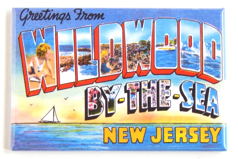 Pode incluir: &Iacute;man de postal vintage com o texto "Greetings From Wildwood By-The-Sea New Jersey". O &iacute;man apresenta uma cena de praia com c&eacute;u azul e oceano, e um veleiro. A palavra "Wildwood" est&aacute; em letras grandes e coloridas.