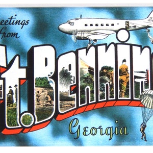Op de afbeelding: Groeten uit Ft. Benning, Georgia ansichtkaart met een blauwe lucht achtergrond en een wit vliegtuig dat erboven vliegt. De ansichtkaart heeft een rode en witte gestileerde tekst "Ft. Benning" met afbeeldingen van soldaten en militair materieel.