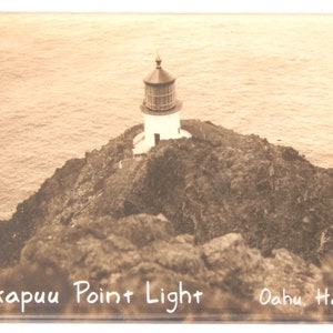 Könnte beinhalten: Ein Schwarzweißfoto eines Leuchtturms auf einer felsigen Klippe mit Blick auf das Meer. Der Leuchtturm ist weiß mit einem schwarzen Dach und einer schwarzen Laterne. Der Text "Makapuu Point Light Oahu, Hawaii" steht unter dem Bild.