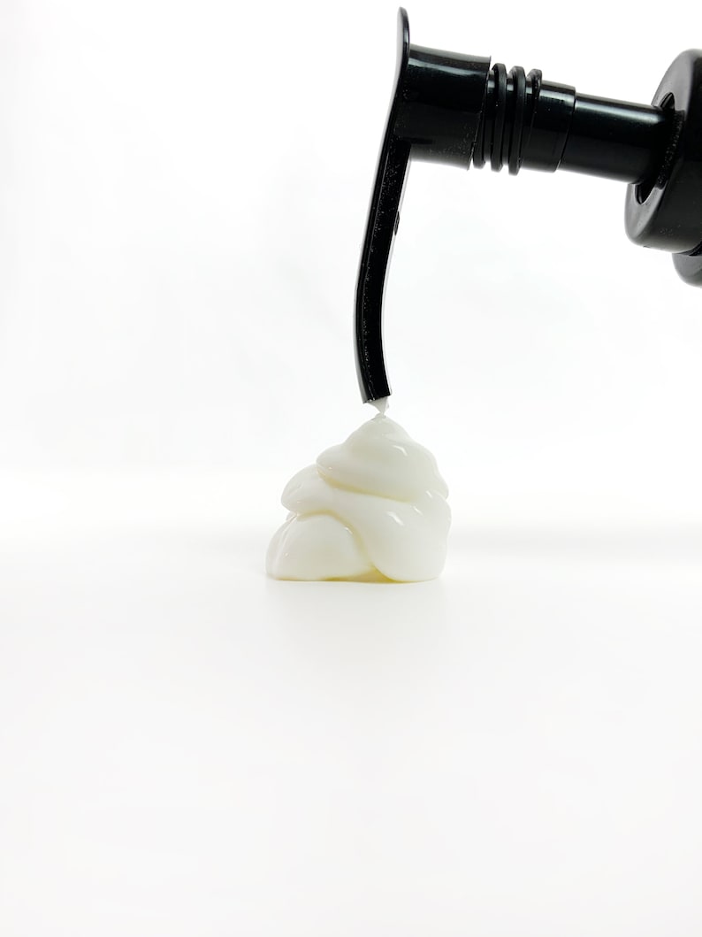 May include: A white creamy substance being dispensed from a black pump bottle. The cream is in a pile on a white surface.