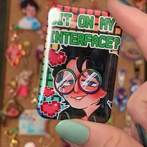 Peut inclure: Épinglette rectangulaire avec le texte "SIT ON MY INTERFACE ?" et une illustration de dessin animé d'une personne avec des lunettes. L'épinglette a un design pixélisé coloré avec des cœurs rouges.