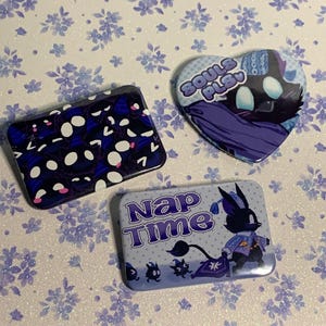 May include: Three pin-back buttons in rectangular and heart shapes. One rectangular button features a dark blue pattern of glowing white eyes. A heart-shaped button displays a dark creature with the text "SOULS PLS". A rectangular button says "Nap Time".