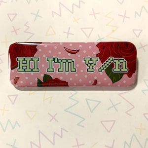 May include: A pink and white button with red roses and white polka dots. The button says "HI I'M Y/N" in green pixelated letters.