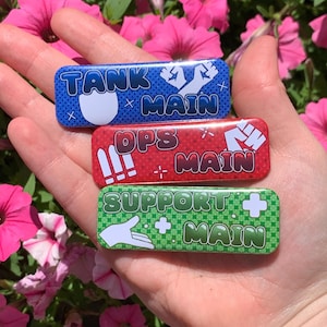 May include: Three rectangular pinback buttons with rounded corners. The top blue button reads TANK MAIN with a fist icon. The middle red button reads OPS MAIN with a fist icon. The bottom green button reads SUPPORT MAIN with a hand icon.