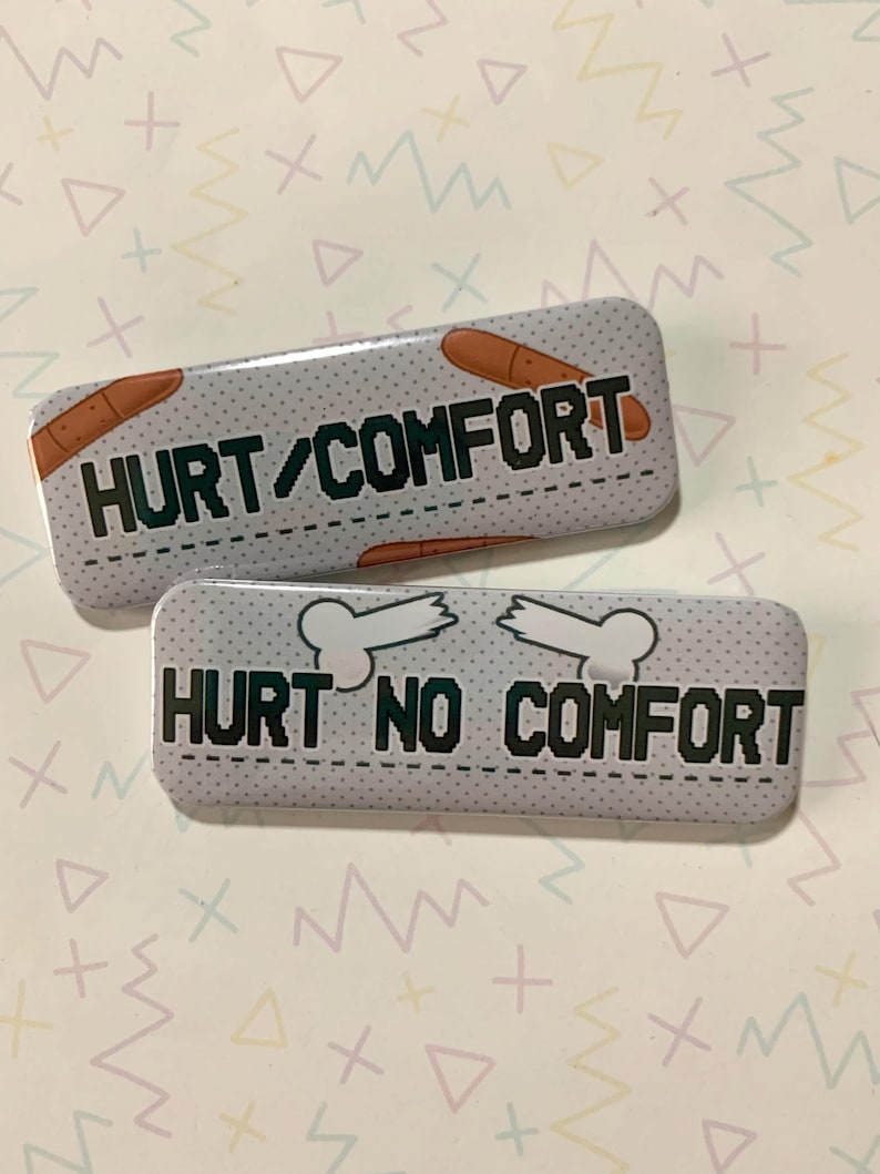 Może przedstawiać: Dwa białe prostokątne guziki z czarnym tekstem i brązowymi grafikami bandaży. G&oacute;rny guzik m&oacute;wi "HURT/COMFORT", a dolny guzik m&oacute;wi "HURT NO COMFORT".