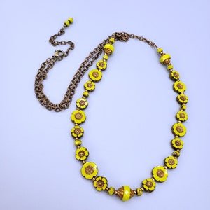 K&ouml;nnte beinhalten: Eine gelbe Blumenkette mit einer goldenen Kette. Die Kette besteht aus Glasperlen mit einem Blumenmuster.