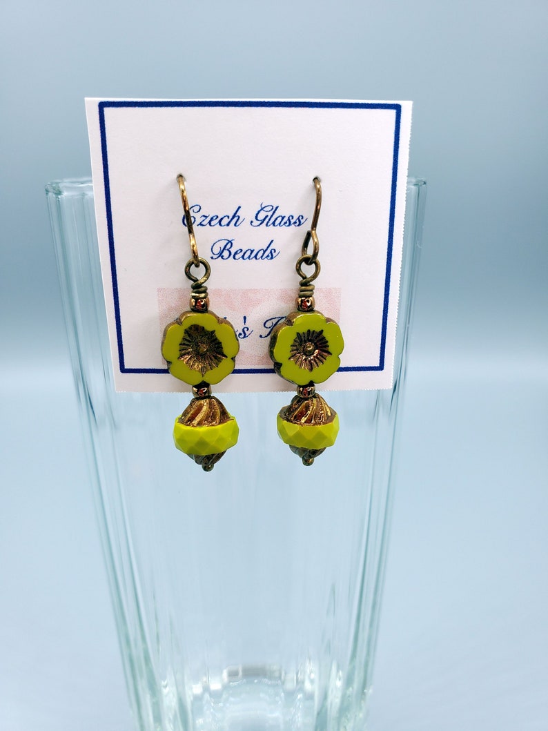 K&ouml;nnte beinhalten: Ein Paar gr&uuml;ne Glasblumenohrringe mit goldenen Akzenten. Die Ohrringe befinden sich auf einer wei&szlig;en Karte mit dem Text "Czech Glass Beads".