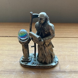 Puede incluir: Una figurita de estaño de un mago sosteniendo un rollo y mirando una bola de cristal. La base de la figurita dice "The Wizard of Infinity".