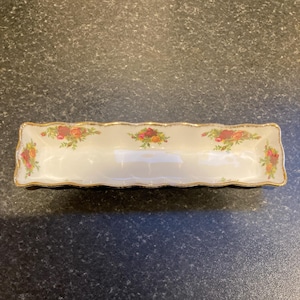 Puede incluir: Un plato rectangular blanco para servir con borde festoneado y ribete dorado. El plato está decorado con un patrón floral en tonos rojos, amarillos y verdes.