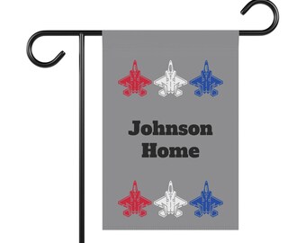 Puede incluir: Una bandera de jardín gris con tres aviones de combate rojo, blanco y azul, el texto "Johnson Home" en negro y tres aviones de combate más en la fila inferior.