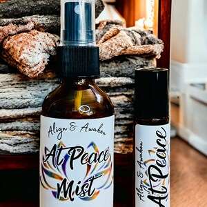 May include: Two bottles of essential oil blend, one in a spray bottle and one in a roller bottle. Both bottles have a white label with the text "Align & Awaken At Peace" and a colorful lotus flower design. The spray bottle is labeled "At Peace Mist" and contains 2 fl oz or 60 ml.