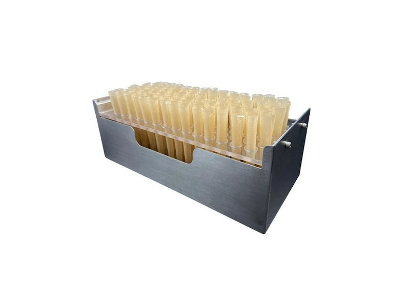 Op de afbeelding: Een metalen container met een transparante kunststof inzet die een groot aantal kleine, beige, cilindrische buizen bevat.