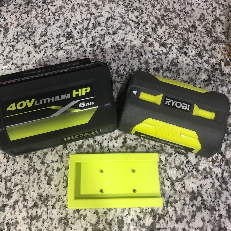 Op de afbeelding: Twee zwarte en gele Ryobi 40V lithium HP batterijen, een met een capaciteit van 6Ah, en een gele plastic batterijhouder.