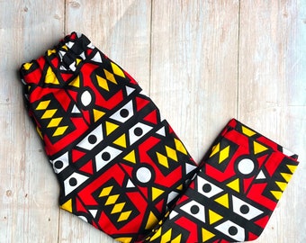 May include: Red, yellow, black, and white patterned pants with a geometric design. The pants have an elastic waistband.