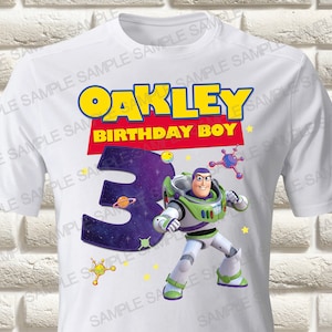 Könnte beinhalten: Weißes T-Shirt mit Buzz Lightyear-Grafik, dem Namen "OAKLEY" über "BIRTHDAY BOY" und einer großen "3" im Weltraum-Design. Gelbe Sterne und Weltraum-Grafiken ergänzen das Design, ideal für einen Geburtstag.