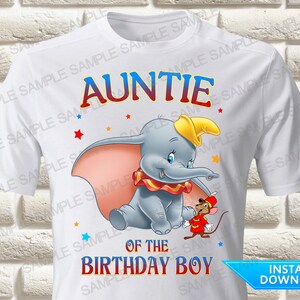 May include: A white short-sleeved t-shirt featuring a graphic of Dumbo the elephant wearing a yellow hat and a red and yellow ruffled collar, standing next to a small mouse in a red circus outfit, with the text AUNTIE OF THE BIRTHDAY BOY.