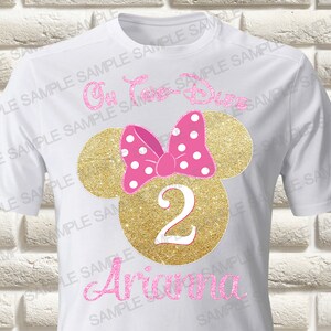 Może przedstawiać: Biała koszulka z głową Minnie Mouse z brokatem w kolorze złotym, z różową kokardką w białe kropki i cyfrą 2 w kolorze różowym. Imię "Ariana" jest napisane różowym kolorem pod cyfrą.