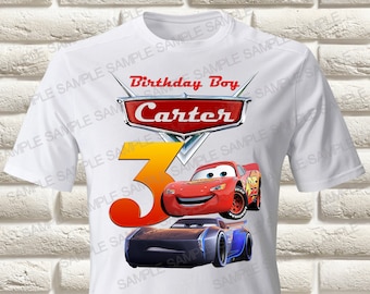 Pode incluir: Camiseta branca com um número 3 vermelho e amarelo, um carro vermelho Lightning McQueen e um carro preto e azul. A camiseta também tem um logotipo vermelho e branco que diz "Birthday Boy Carter".