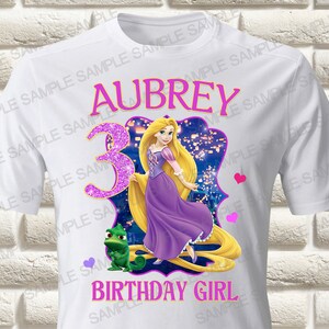 May include: White t-shirt with a purple and gold image of Rapunzel from the Disney movie Tangled. The shirt also has the text "Aubrey" and "Birthday Girl" in pink.